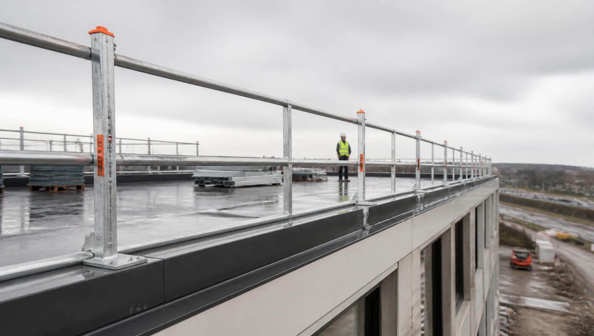 Stalen dakrandbeveiliging met leuningen langs een platte dakrand op een bouwplaats